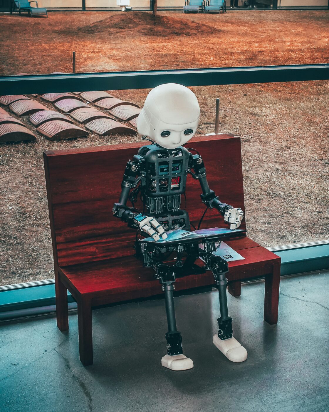 Robot sat on bench using a laptop to do a Google search